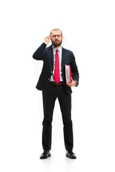 Full body or full-length portrait of businessman with red folder on white studio background. Serious bearded young man in glasses, suit, red tie standing in office. Business, career, success concept.