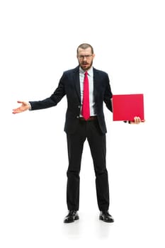 Full body or full-length portrait of businessman with red folder on white studio background. Angry bearded young man in glasses, suit, red tie standing in office. Business, career, success concept.