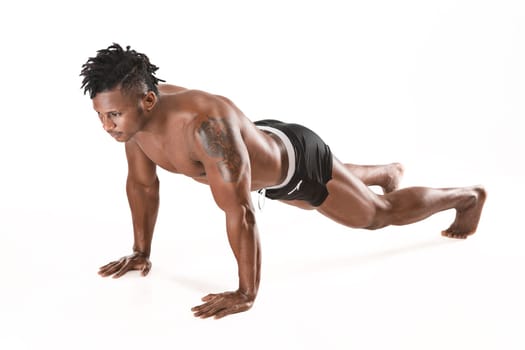Muscular young man doing press-ups. Fit young man with beautiful torso, isolated on white background. The naked torso of African American man.The muscular body, fitness, sports, healthy lifestyle and bodybuilder concept.