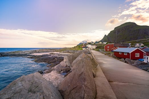 Village of Reine on Lofoten islands in Norway. Traditional red wooden houses and mountains. Sunset sky with clouds. Travel in Scandinavia, Europe.
