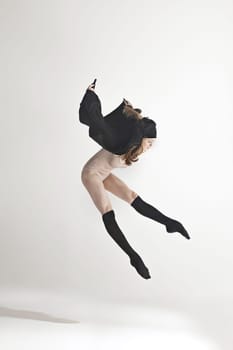 Young beautiful dancer in beige swimsuit dancing on gray studio background. Front view. Young female classical ballet dancer. Ballerina project. Modern choreography, contemporary. Fit caucasian moman