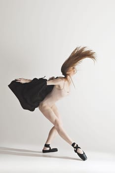 Young beautiful dancer in beige swimsuit dancing on gray studio background. Front view. Young female classical ballet dancer. Ballerina project. Modern choreography, contemporary. Fit caucasian moman