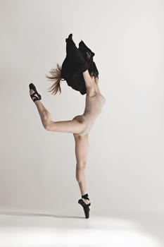 Young beautiful dancer in beige swimsuit dancing on gray studio background. Front view. Young female classical ballet dancer. Ballerina project. Modern choreography, contemporary. Fit caucasian moman