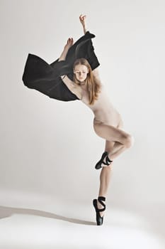 Young beautiful dancer in beige swimsuit dancing on gray studio background. Front view. Young female classical ballet dancer. Ballerina project. Modern choreography, contemporary. Fit caucasian moman