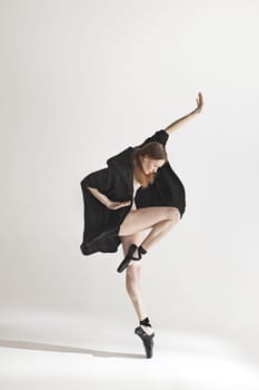 Young beautiful dancer in beige swimsuit dancing on gray studio background. Front view. Young female classical ballet dancer. Ballerina project. Modern choreography, contemporary. Fit caucasian moman
