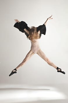 Young beautiful dancer in beige swimsuit dancing on gray studio background. Front view. Young female classical ballet dancer. Ballerina project. Modern choreography, contemporary. Fit caucasian moman