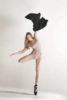 Young beautiful dancer in beige swimsuit dancing on gray studio background. Front view. Young female classical ballet dancer. Ballerina project. Modern choreography, contemporary. Fit caucasian moman