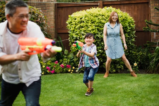 Family are having a water fight in the garden with pistols.