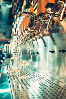 The beer taps in a pub. nobody. Selective focus. Alcohol concept. Vintage style. Beer craft. Bar table. Steel taps. Shiny taps. Glass of beer