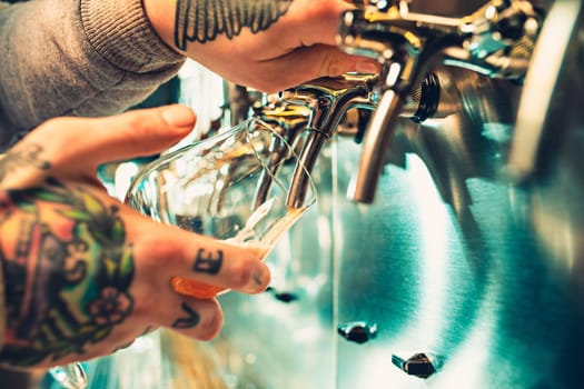 Hand of bartender pouring a large lager beer in tap. Soft, vintage instagram effect on photo. Pouring beer for client. Side view of young bartender pouring beer while standing at the bar counter
