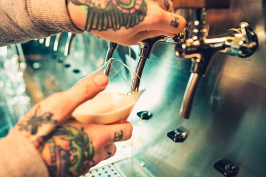 Hand of bartender pouring a large lager beer in tap. Soft, vintage instagram effect on photo. Pouring beer for client. Side view of young bartender pouring beer while standing at the bar counter