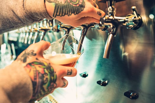 Hand of bartender pouring a large lager beer in tap. Soft, vintage instagram effect on photo. Pouring beer for client. Side view of young bartender pouring beer while standing at the bar counter