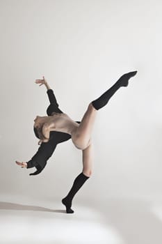 Young beautiful dancer in beige swimsuit dancing on gray studio background. Front view. Young female classical ballet dancer. Ballerina project. Modern choreography, contemporary. Fit caucasian moman