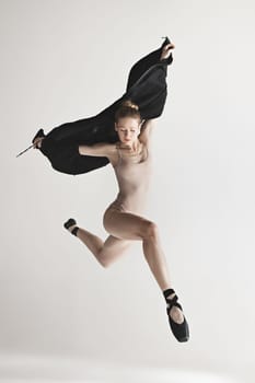 Young beautiful dancer in beige swimsuit dancing on gray studio background. Front view. Young female classical ballet dancer. Ballerina project. Modern choreography, contemporary. Fit caucasian moman