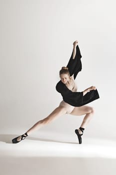 Young beautiful dancer in beige swimsuit dancing on gray studio background. Front view. Young female classical ballet dancer. Ballerina project. Modern choreography, contemporary. Fit caucasian moman