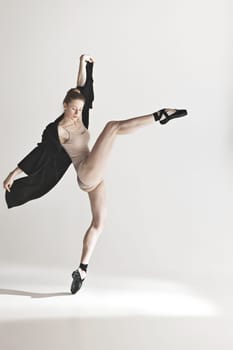 Young beautiful dancer in beige swimsuit dancing on gray studio background. Front view. Young female classical ballet dancer. Ballerina project. Modern choreography, contemporary. Fit caucasian moman