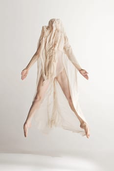 Young beautiful dancer in beige swimsuit dancing on gray studio background. Front view. Young female classical ballet dancer. Ballerina project. Modern choreography, contemporary. Fit caucasian moman