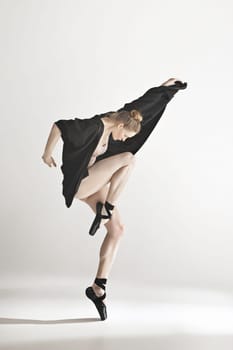 Young beautiful dancer in beige swimsuit dancing on gray studio background. Front view. Young female classical ballet dancer. Ballerina project. Modern choreography, contemporary. Fit caucasian moman