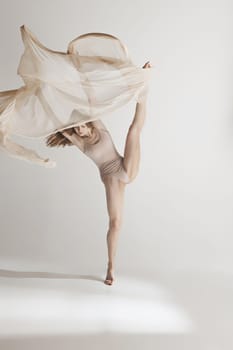 Young beautiful dancer in beige swimsuit dancing on gray studio background. Front view. Young female classical ballet dancer. Ballerina project. Modern choreography, contemporary. Fit caucasian moman