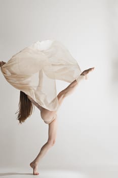 Young beautiful dancer in beige swimsuit dancing on gray studio background. Front view. Young female classical ballet dancer. Ballerina project. Modern choreography, contemporary. Fit caucasian moman