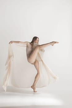 Young beautiful dancer in beige swimsuit dancing on gray studio background. Front view. Young female classical ballet dancer. Ballerina project. Modern choreography, contemporary. Fit caucasian moman