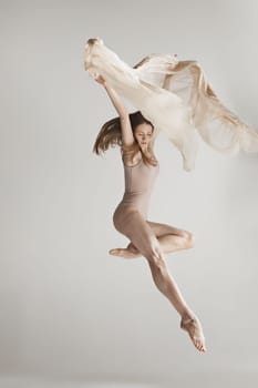 Young beautiful dancer in beige swimsuit dancing on gray studio background. Front view. Young female classical ballet dancer. Ballerina project. Modern choreography, contemporary. Fit caucasian moman