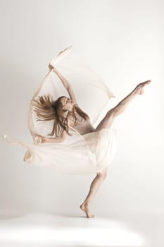 Young beautiful dancer in beige swimsuit dancing on gray studio background. Front view. Young female classical ballet dancer. Ballerina project. Modern choreography, contemporary. Fit caucasian moman