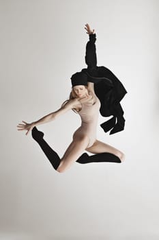 Young beautiful dancer in beige swimsuit dancing on gray studio background. Front view. Young female classical ballet dancer. Ballerina project. Modern choreography, contemporary. Fit caucasian moman