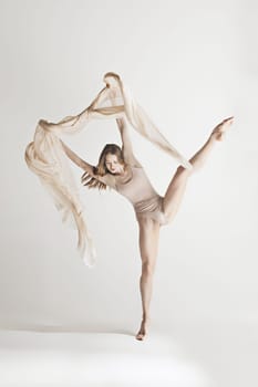 Young beautiful dancer in beige swimsuit dancing on gray studio background. Front view. Young female classical ballet dancer. Ballerina project. Modern choreography, contemporary. Fit caucasian moman