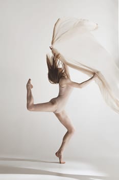 Young beautiful dancer in beige swimsuit dancing on gray studio background. Front view. Young female classical ballet dancer. Ballerina project. Modern choreography, contemporary. Fit caucasian moman