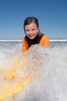 Little girl is smiling for the camera as she bodyboards in the sea.