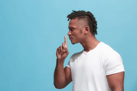 Secret, gossip concept. Young man whispering a secret behind his hand. Businessman isolated on trendy blue studio background. Young emotional man. Human emotions, facial expression concept. afro-american. profile