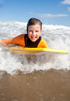 Little girl is smiling for the camera as she bodyboards in the sea.