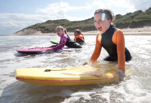 Three girls are bodyboarding in the sea together.