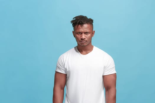 Angry, hate, rage. Emotional angry afro man on blue studio background. Emotional, young face. Front male half-length portrait. Human emotions, facial expression concept. Trendy colors