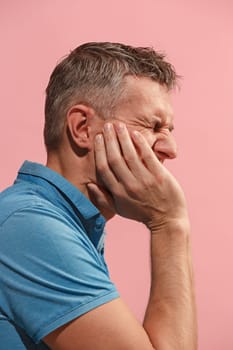 Young man is having toothache. Pain concept. Young emotional man. Human emotions, facial expression concept. Studio. Isolated on trendy pink color
