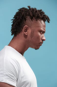 Angry, hate, rage. Emotional angry afro man on blue studio background. Emotional, young face. Profile male half-length portrait. Human emotions, facial expression concept. Trendy colors