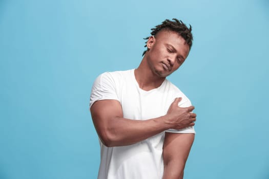 Pain concept. Beautiful afro male portrait isolated on blue backgroud. Young emotional surprised man looking at camera.Human emotions, facial expression concept. man overwhelmed with pain in shoulder