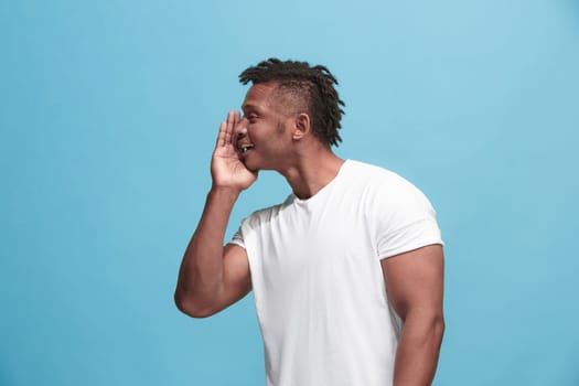 Secret, gossip concept. Young man whispering a secret behind his hand. Businessman isolated on trendy blue studio background. Young emotional man. Human emotions, facial expression concept. afro-american. profile