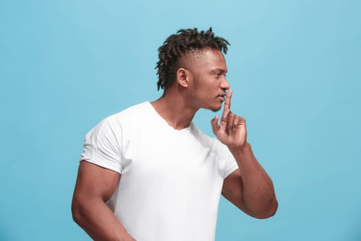 Secret, gossip concept. Young man whispering a secret behind his hand. Businessman isolated on trendy blue studio background. Young emotional man. Human emotions, facial expression concept. afro-american. profile