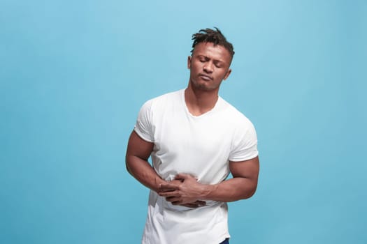Pain concept. Beautiful male portrait isolated on blue backgroud. Young emotional surprised man looking at camera.Human emotions, facial expression concept. man overwhelmed with pain in stomach