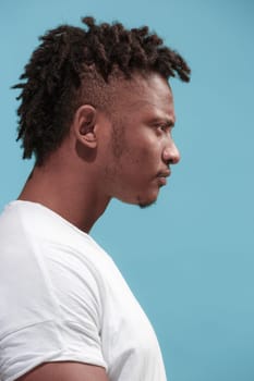 Angry, hate, rage. Emotional angry afro man on blue studio background. Emotional, young face. Profile male half-length portrait. Human emotions, facial expression concept. Trendy colors