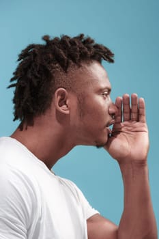 Secret, gossip concept. Young man whispering a secret behind his hand. Businessman isolated on trendy blue studio background. Young emotional man. Human emotions, facial expression concept. afro-american. profile