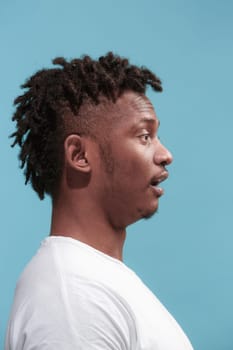 Surprised business Afro-American man standing and looking isolated on blue studio background. African American male profile portrait. Young emotional man. The human emotions, facial expression concept.