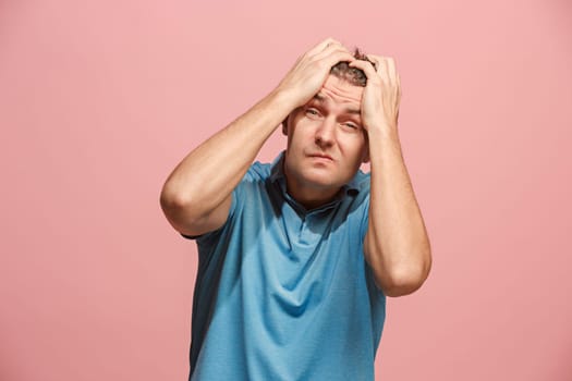 Horrible, stress, shock. Male half-length portrait isolated at pink studio. Young emotional surprised man clasping head in hands. Human emotions, facial expression concept. Trendy colors. Front view