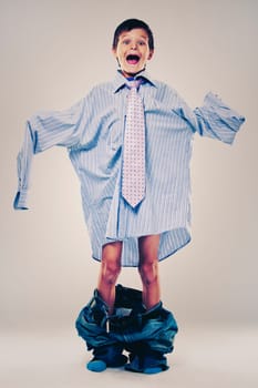Caucasian boy wearing his Dad's shirt, jeans and tie on light background. He is wearing big adult size clothes which are too big for him.