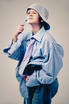 Caucasian boy wearing his Dad's shirt, jeans and tie on light background. He is wearing big adult size clothes which are too big for him.