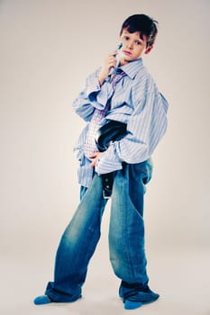 Caucasian boy wearing his Dad's shirt, jeans and tie on light background. He is wearing big adult size clothes which are too big for him.