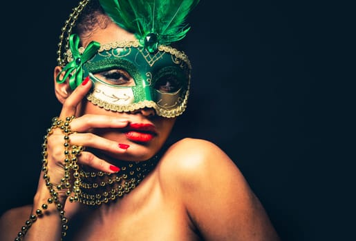 Upscale Indian woman wearing gold jewellery and red lipstick on black background. Green party mask.