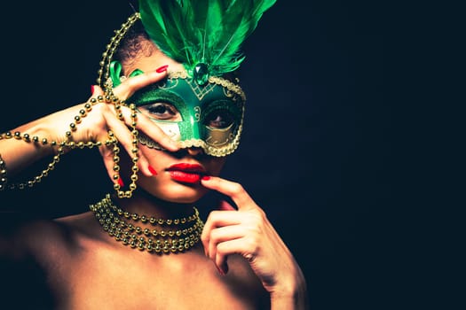 Upscale Indian woman wearing gold jewellery and red lipstick on black background. Green party mask.